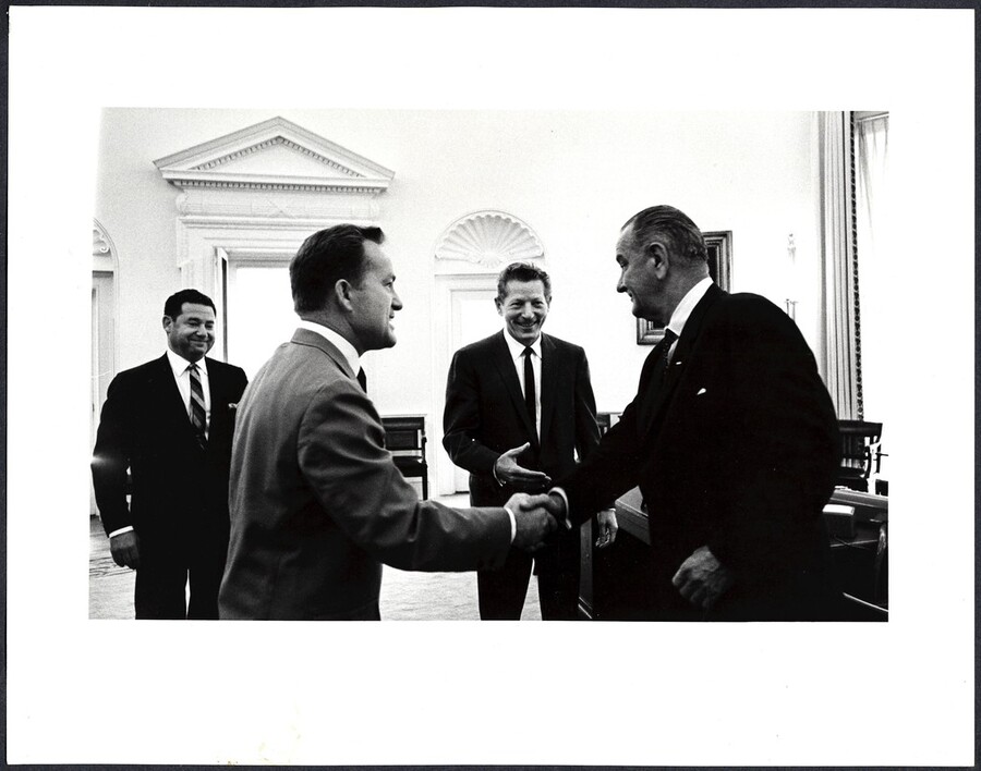 [ Sargent Shriver shakes hands with Lyndon Johnson in the Oval Office. Danny Kaye and unknown man stand in the background]